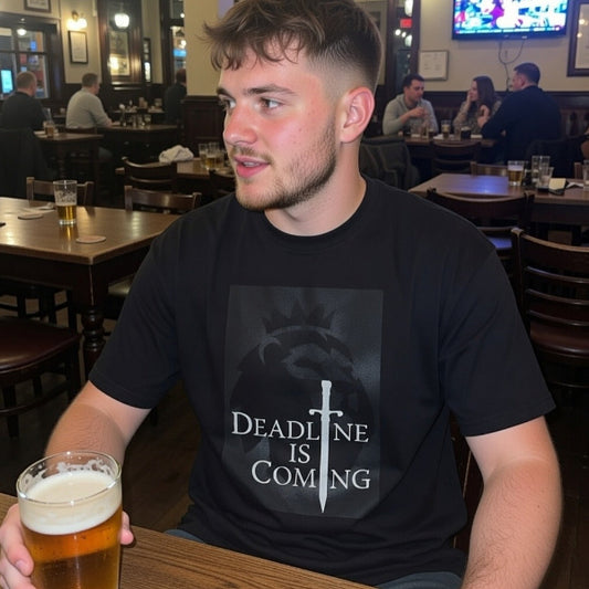 Man sitting at a bar with a beer, wearing a black t-shirt with 'Deadline is Coming' text.