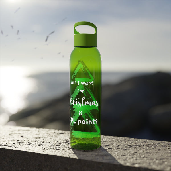 A translucent green water bottle with a matching green loop cap stands on a stone ledge outdoors, with a blurred coastal or rocky background. The bottle has white text that reads, 'All I want for Christmas is FPL points.