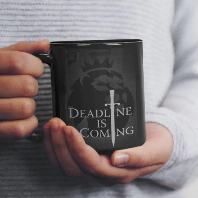 Person holding a black mug with 'Deadline is Coming' design