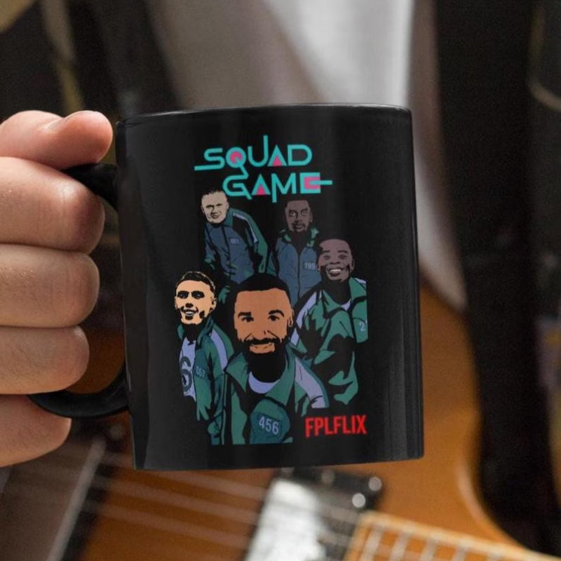 Black mug with 'Squad Game' design featuring illustrated characters, held by a hand.