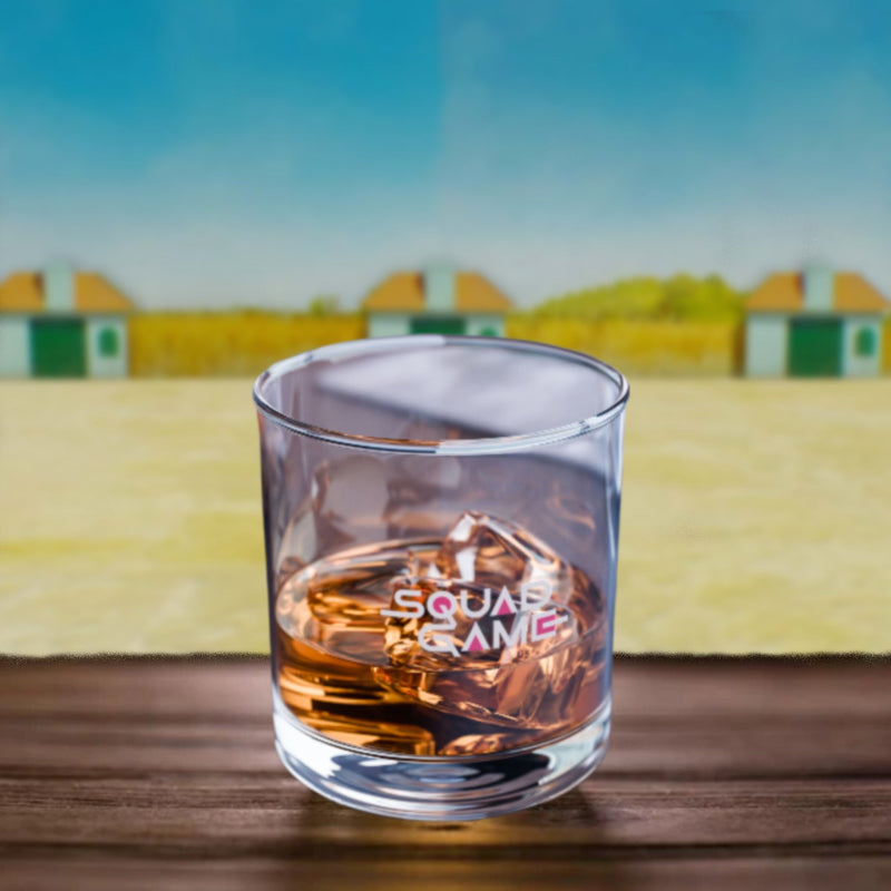 Glass of whiskey with 'Squad Game' logo on a wooden surface with a scenic background