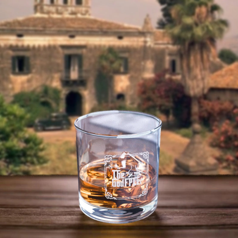 Glass of whiskey with 'The Old Rye' branding on a wooden surface with a blurred background of a building and trees.
