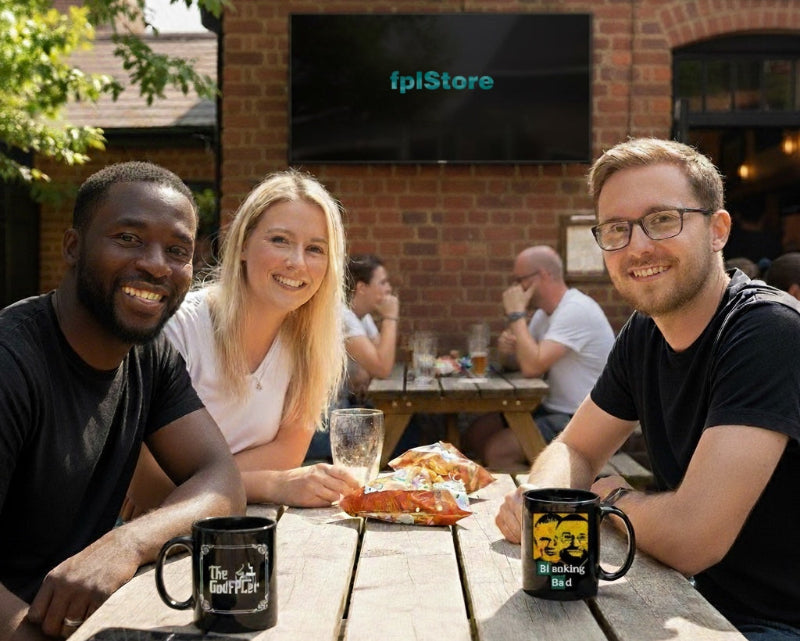 Three people sitting at a wooden table outdoors with a TV displaying 'fpiStore' in the background.