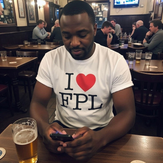 Man sitting at a bar wearing a 'I ❤️ FPL' shirt, looking at his phone.