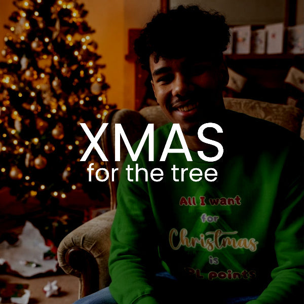 A smiling man wearing a green Christmas sweatshirt with the text 'XMAS for the tree' and 'All I want for Christmas is 31 points' in a cozy living room setting with a lit Christmas tree in the background.