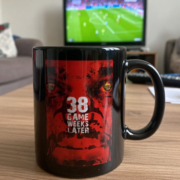 Black mug with red design and text on a table in a living room setting.
