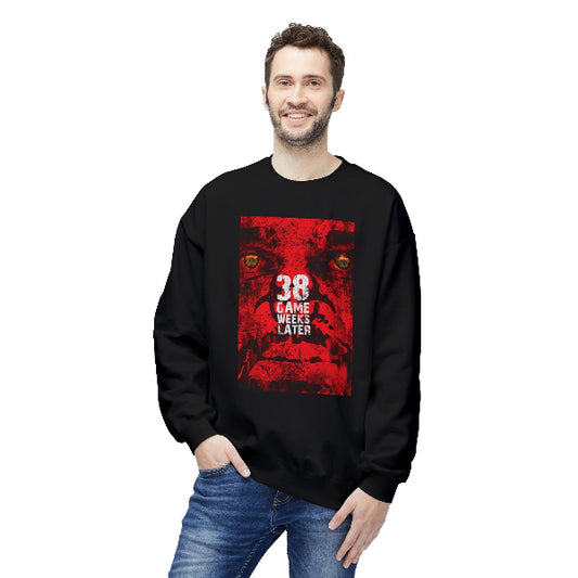 A man wearing a black crewneck sweatshirt with a red graphic print on the front that reads '38 GAME WEEKS LATER' with two soccer player silhouettes, paired with blue jeans, against a plain white background.
