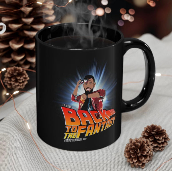 A black ceramic mug with a custom 'Back to the Fantasy' graphic print, shown with steam rising from hot coffee inside. The mug is styled on a light gray textured fabric surrounded by pinecones and fairy lights.