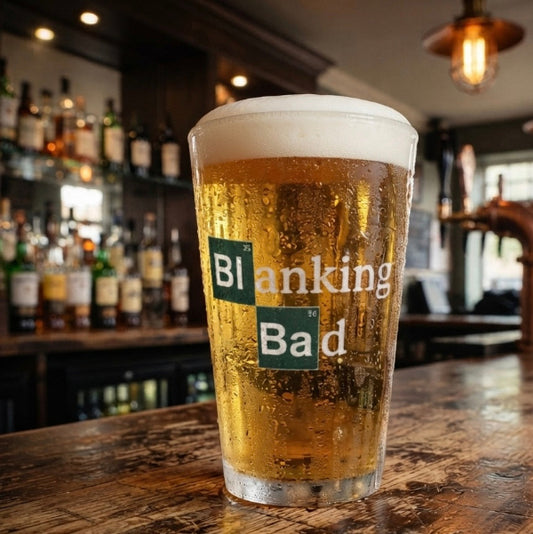A pint of golden beer with a thick white foam head sits on a rustic wooden bar counter in a dimly lit pub. The clear glass features a white and green graphic that reads 'Blanking Bad'.