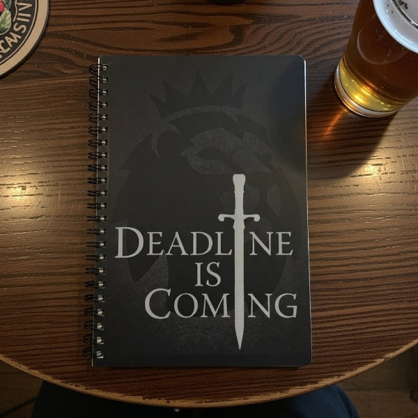 Notebook with 'Deadline is Coming' design on a wooden table with a drink.