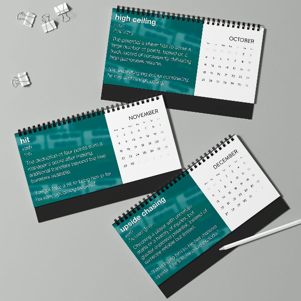 Three spiral-bound desk calendar pages arranged on a light gray surface, showing January, February, and March with teal and white panels and black text. A white pen and small binder clips are placed nearby as props.