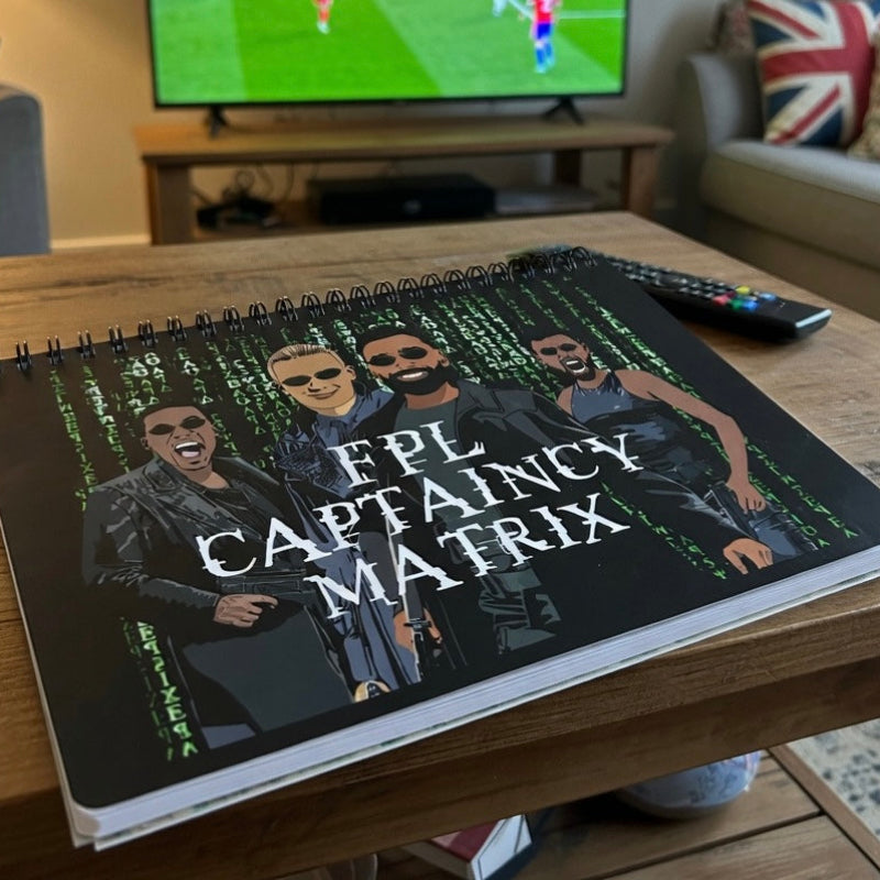 Notebook titled 'FPL Captaincy Matrix' on a table with a TV in the background