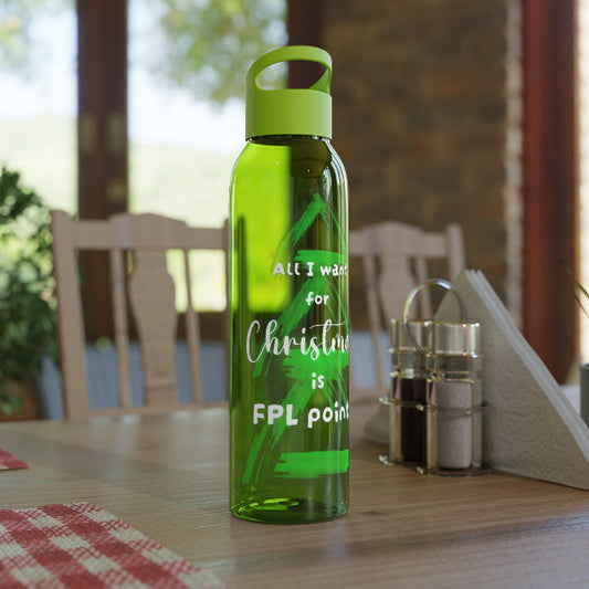 A translucent green water bottle with a matching green loop cap stands on a wooden dining table in a real indoor setting with chairs, windows, and table accessories visible in the background.