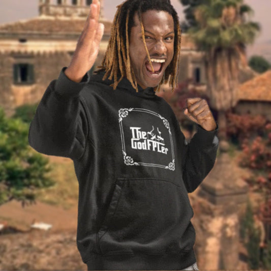 Person wearing a black hoodie with 'The Godfather' logo, standing in front of a rustic building and trees.