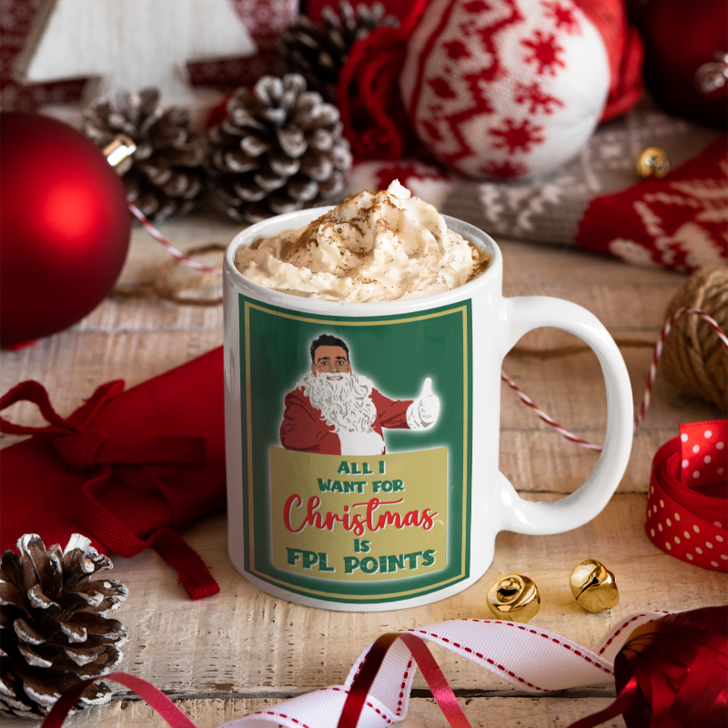 Mug with Santa Claus design and whipped cream, surrounded by Christmas decorations on a wooden surface.