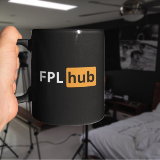 Black mug with FPL hub logo held in a hand, blurred indoor background