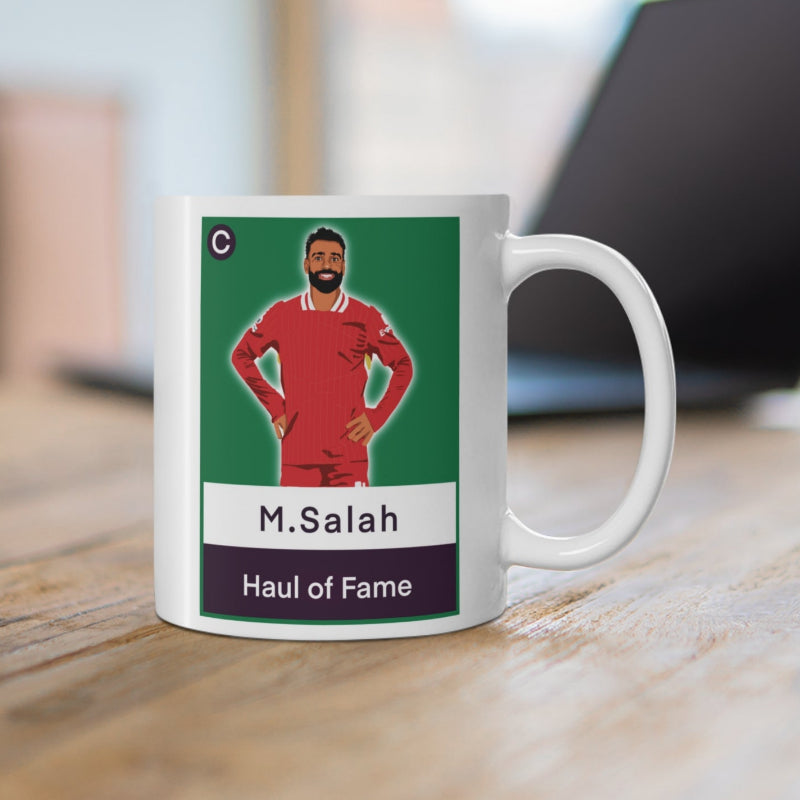 Mug with a graphic of a person in a red sports uniform on a green background, placed on a wooden surface.