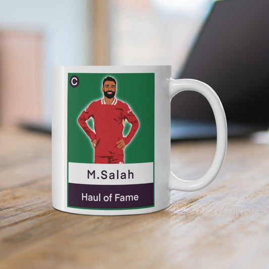 Mug with a graphic of a person in a red sports uniform on a green background, placed on a wooden surface.