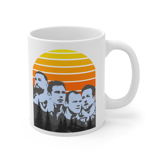 White mug with a design of four silhouettes against an orange and yellow sunset, on a white background.