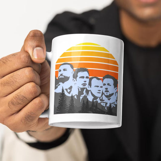Person holding a mug with a design of four faces and a sunset