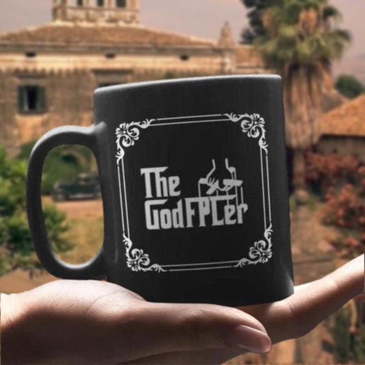 Black mug with 'The GodFPLer' design held in front of a blurred outdoor background