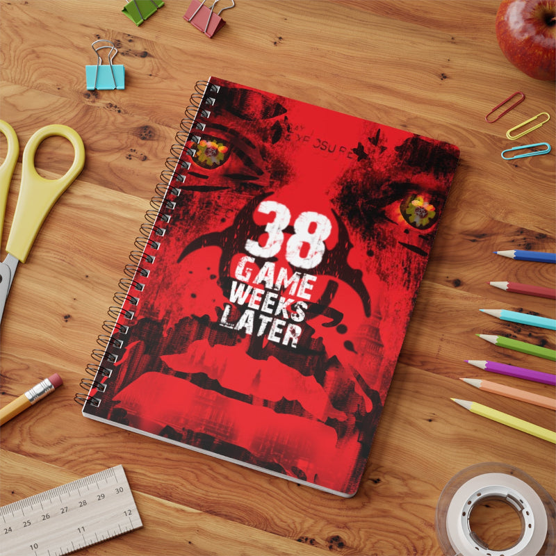 Notebook with '38 Game Weeks Later' design on a wooden surface with stationery items.