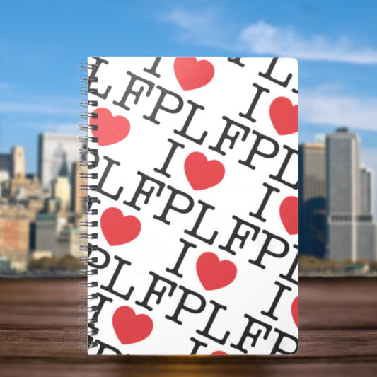 Notebook with 'I ❤️ FPL' pattern on a wooden surface with a cityscape background