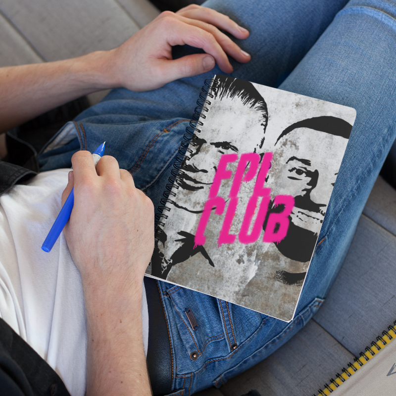 Person holding a notebook with 'FPL Club' design on a couch