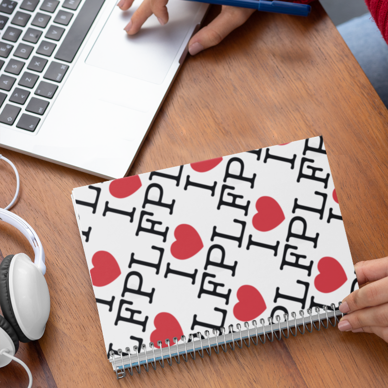 Person using a laptop with a notebook labelled 'I love FPL' on a desk.