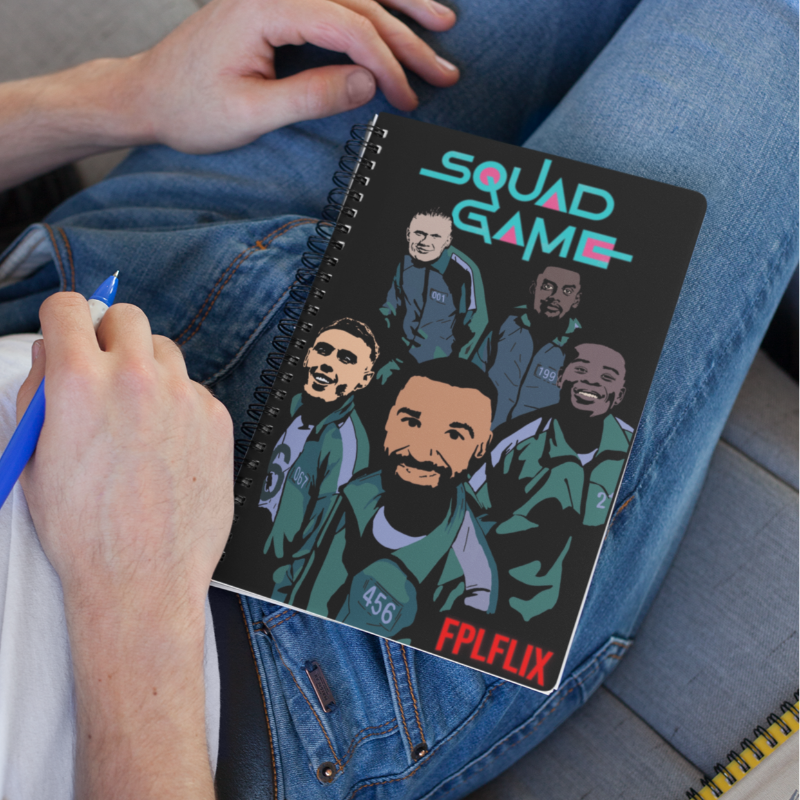 Person holding a notebook with 'Squad Game' design on a couch