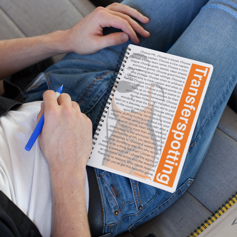 Person sitting on a couch with a notebook titled 'Transferspotting' and a pen.