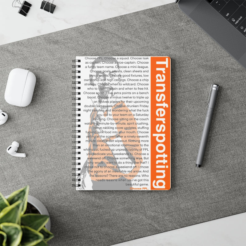 Notebook with 'Transferspotting' cover on a desk with a pen and airpods.