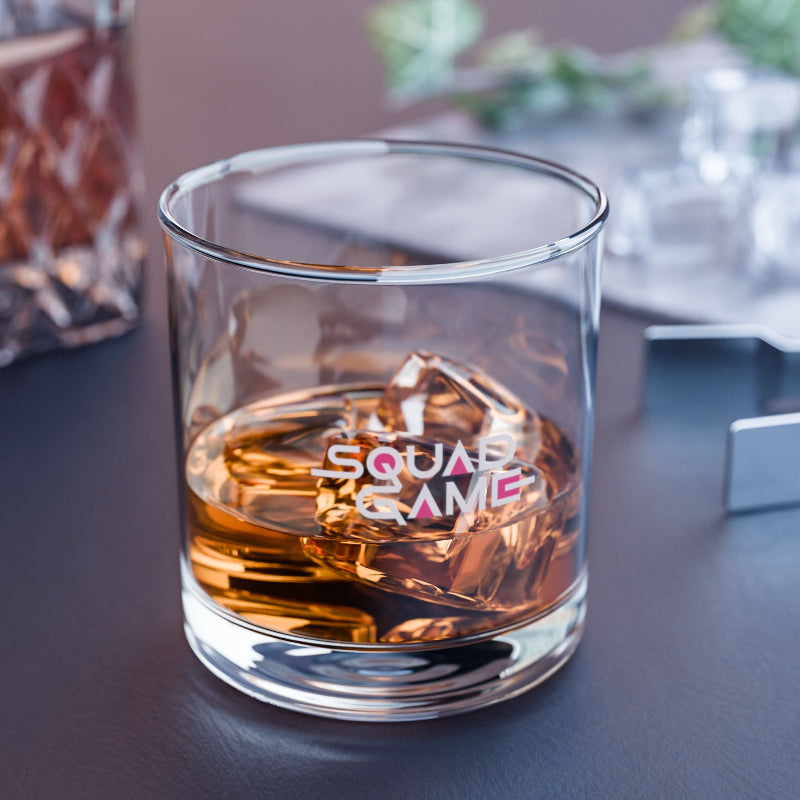 Glass of whiskey with ice cubes and 'SQUAD GAME' text on a table.