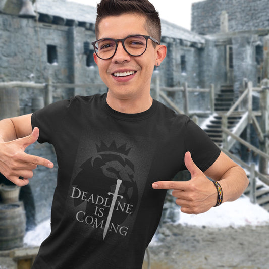 Person wearing a black t-shirt with a logo and text, standing in front of a stone building.