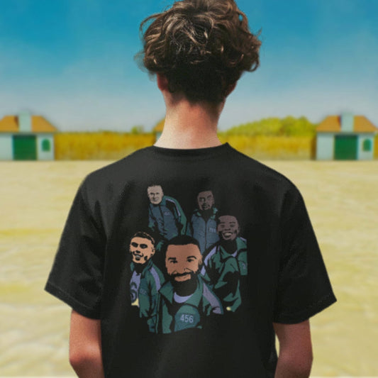 Person wearing a black t-shirt with graphic design of five men on the back, standing in an open area with buildings in the background.