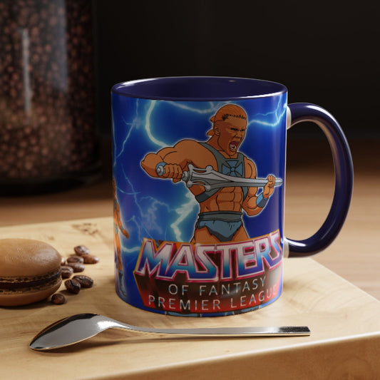 A ceramic coffee mug featuring a vibrant graphic of Masters of the Universe He-Man with lightning effects and the text 'MASTERS OF FANTASY PREMIER LEAGUE'. The mug is set on a wooden board with a spoon and a macaron, with a blurred background of coffee beans.