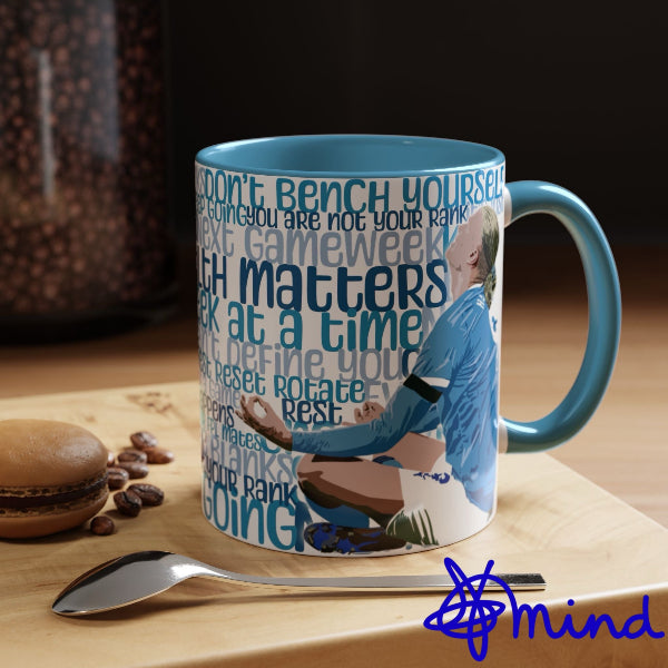 Mug with motivational quote and sports-themed design on a wooden surface with coffee beans and a spoon.