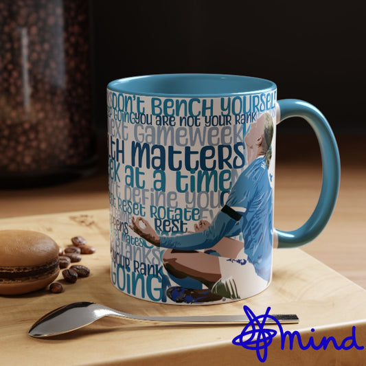 Mug with motivational quote and sports-themed design on a wooden surface with coffee beans and a spoon.