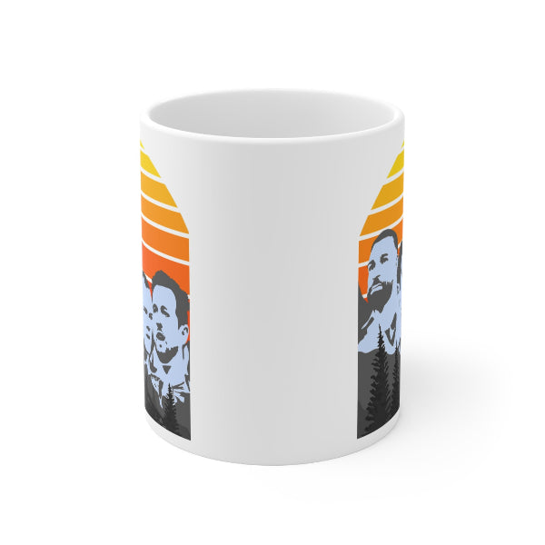 A white ceramic mug featuring a stylized graphic print of two men's faces in black and light blue, set against a retro sunset background with orange, yellow, and red stripes.