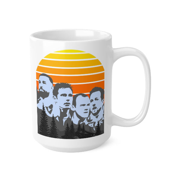 A white ceramic mug featuring a stylized graphic print of the five Mount Rushmore presidents in blue-gray against a retro sunset background with yellow, orange, and red stripes, and dark pine trees at the bottom.