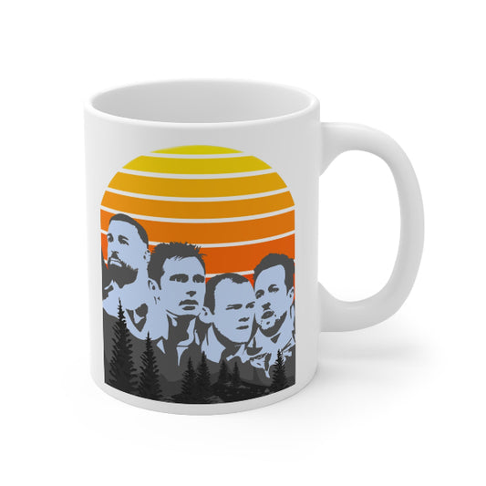 A white ceramic coffee mug featuring a stylized graphic print of the band Soundgasm, showing their faces in blue-gray against a retro sunset background with yellow, orange, and red stripes and pine trees.