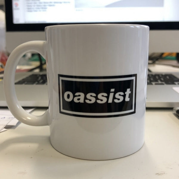 White mug with 'oassist' logo on a desk with a computer in the background