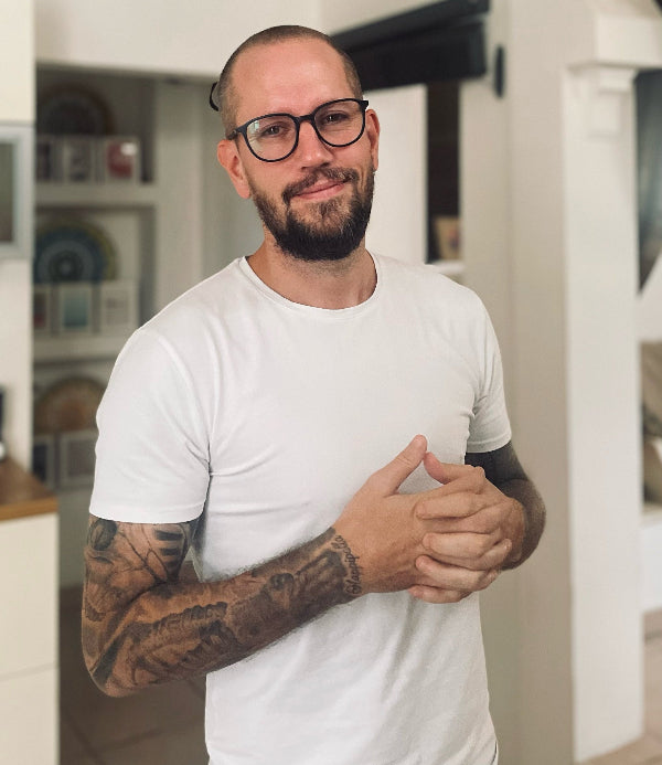 Man with tattoos and glasses wearing a white t-shirt indoors
