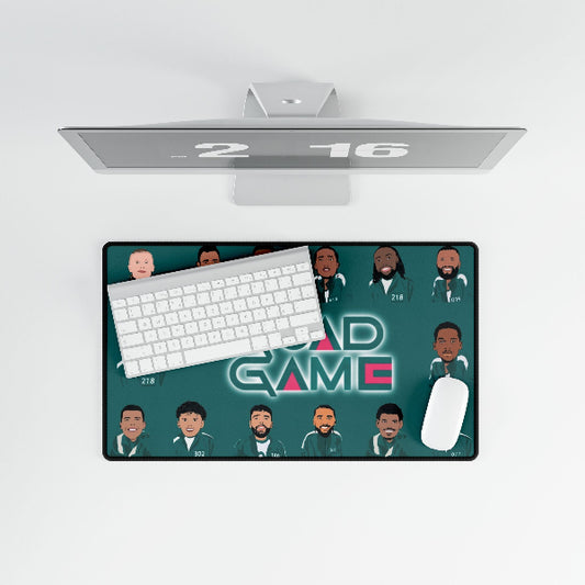 A rectangular desk mat with a dark teal background, cartoon-style illustrated avatars, and the words 'AD GAME' in stylized neon lettering, shown under a computer monitor with a keyboard and mouse on a light gray background.