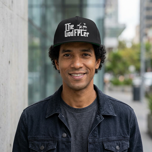 A smiling man wearing a black baseball cap with 'The Godf***er' printed in white across the front, photographed outdoors against a softly blurred urban background.