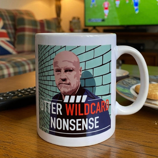 Mug with a graphic design of a man against a brick wall and text, placed on a table in a living room setting.